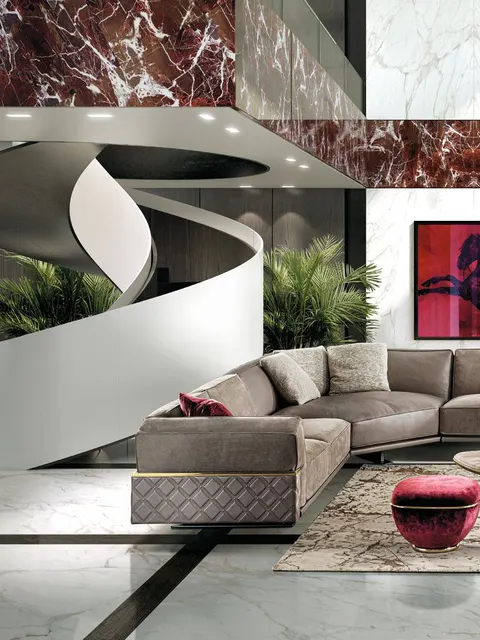 Divano curvo Longhi grigio accanto a una scala scultorea con pouf rosso, design di soggiorno per villa moderna