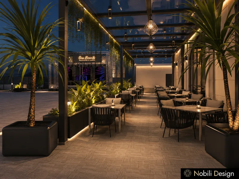 Covered event venue terrace with rope chairs, lit planters, palms and hanging lanterns under a glass roof at night