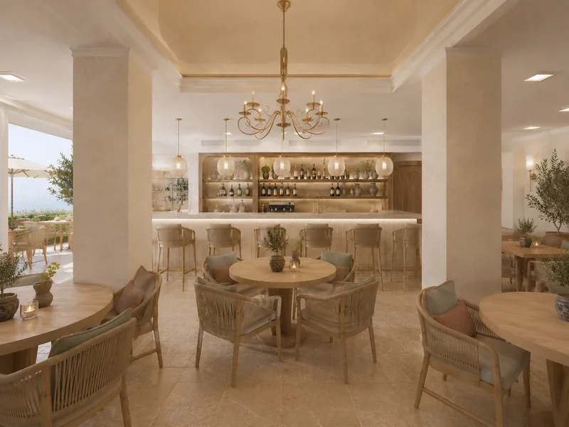 Mediterranean restaurant with round oak tables, woven armchairs and a brass chandelier in front of a lit bar